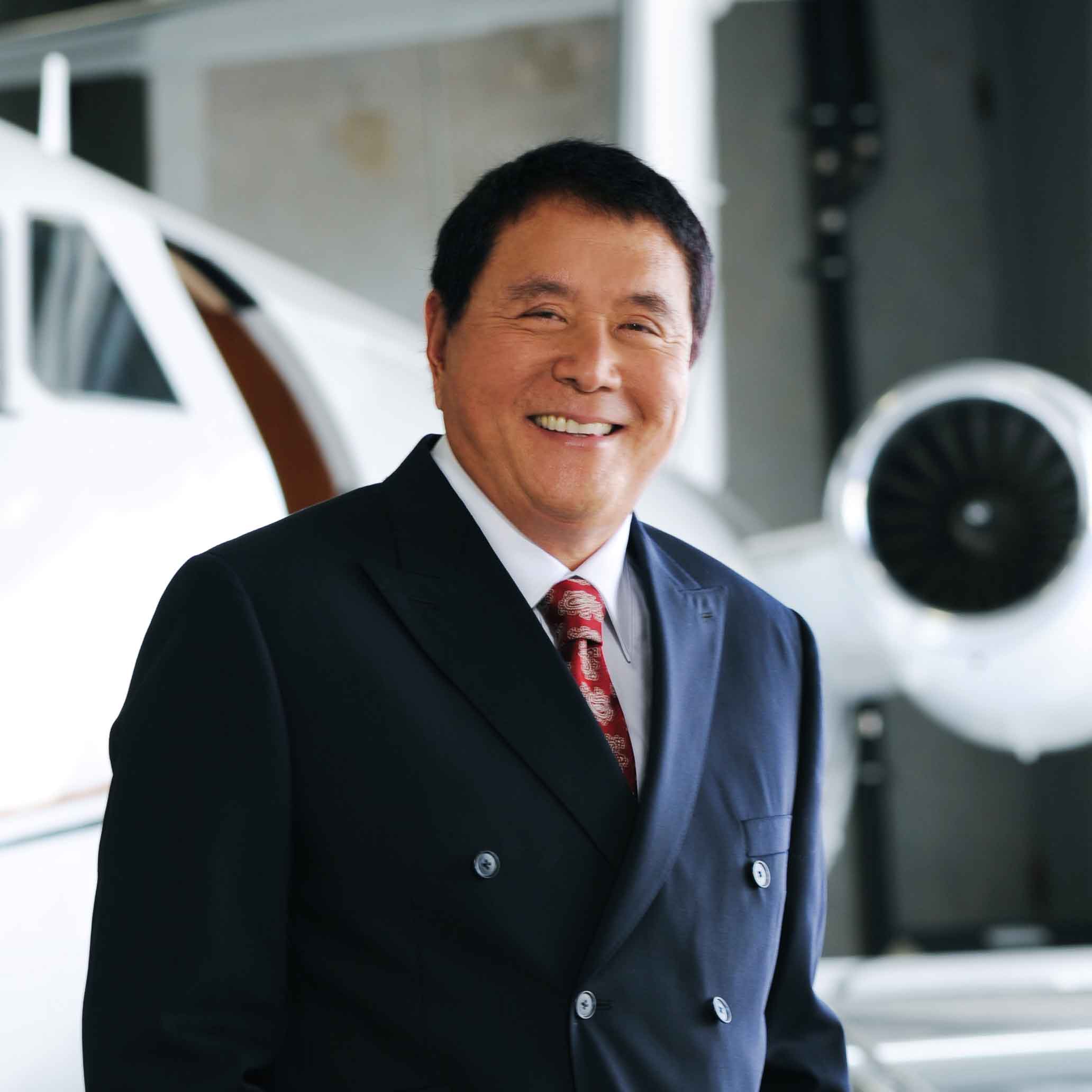 Robert Kiyosaki standing by a private jet in an airplane hanger.